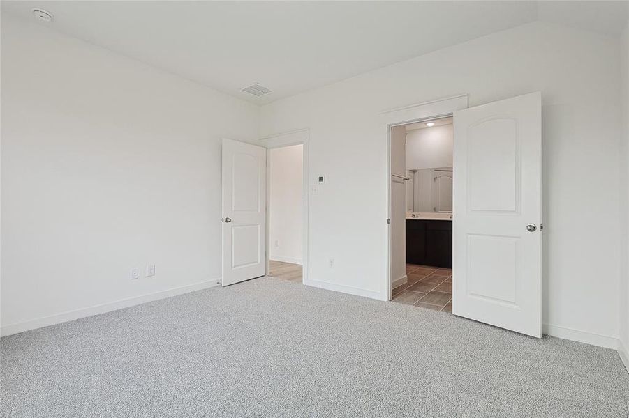 Unfurnished bedroom featuring light carpet, vaulted ceiling, and ensuite bathroom