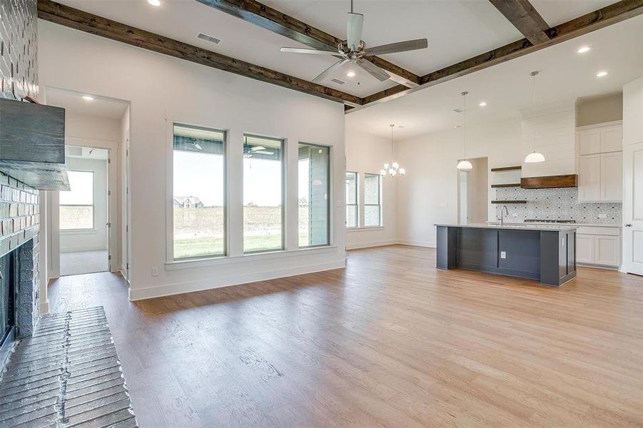 Unfurnished living room with ceiling fan with notable chandelier, light hardwood / wood-style flooring, a brick fireplace, beam ceiling, and sink