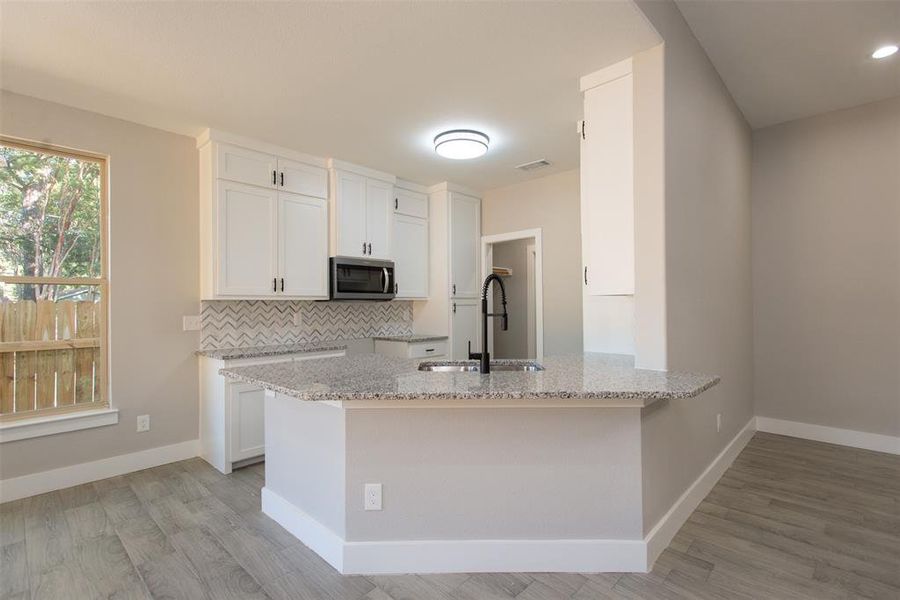 Kitchen with light stone counters, white cabinets, sink, kitchen peninsula, and light wood-type flooring