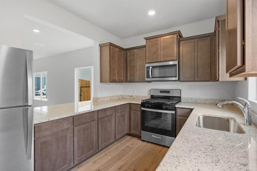 Kitchen with appliances with stainless steel finishes, light stone counters, kitchen peninsula, light wood-style flooring, and sink