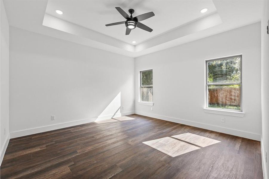 Empty room with dark wood-type flooring, a tray ceiling, and ceiling fan