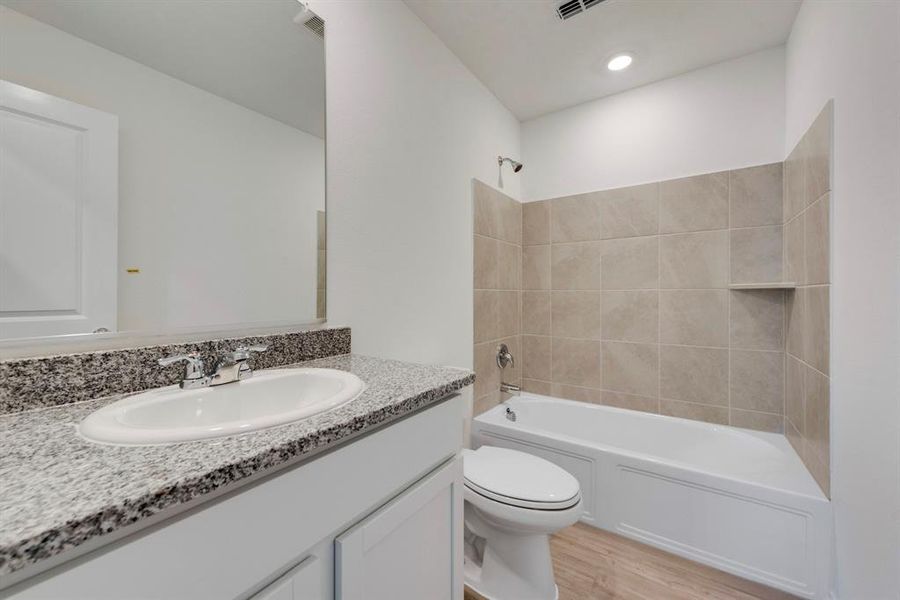 Full bathroom with vanity, tiled shower / bath combo, hardwood / wood-style flooring, and toilet