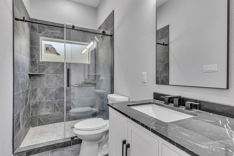 Bathroom featuring a shower with door, vanity, tile patterned floors, and toilet