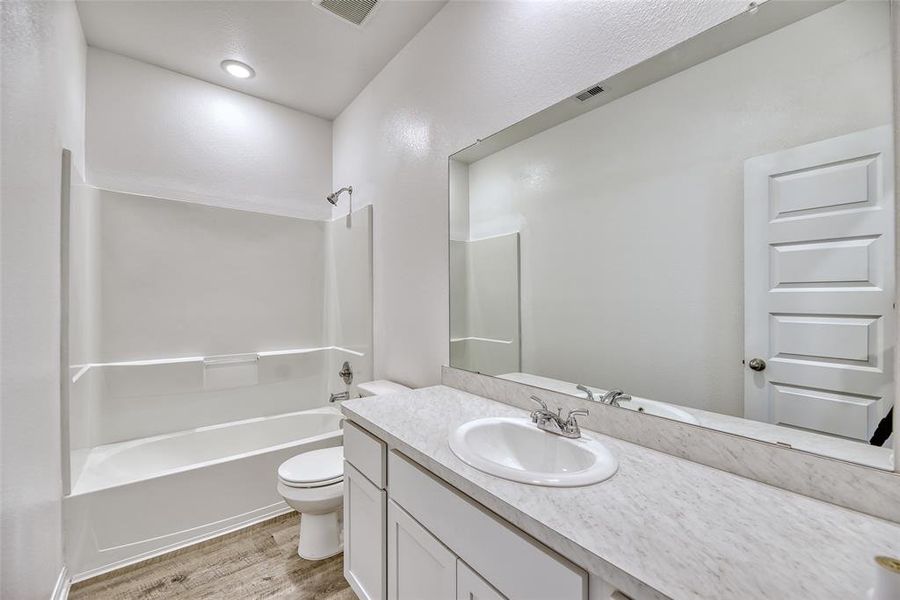 The secondary bathroom offers a spacious counter with ample drawers and cabinets, ideal for shared use. A large frameless mirror hangs above the vanity, enhancing the room's spacious feel and functionality. An oversized tub/shower combination stands ready for relaxation or quick refreshment.