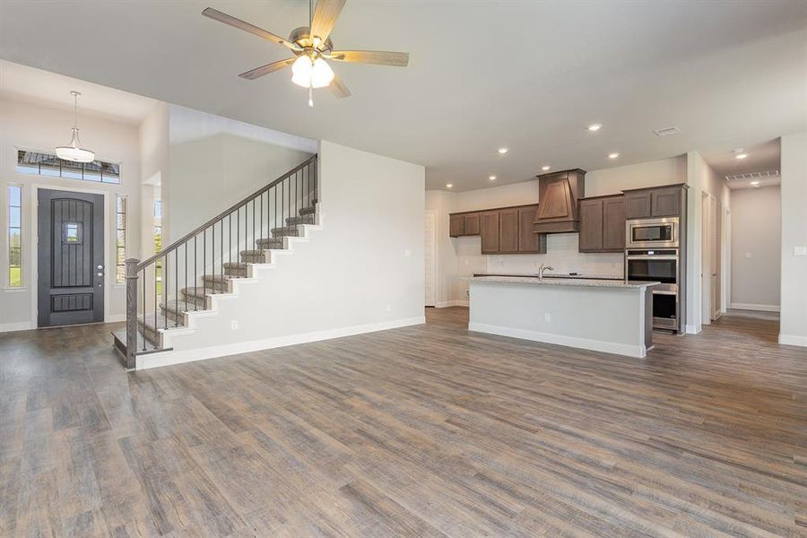 Kitchen with dark wood-type flooring, ceiling fan, stainless steel microwave, and custom range hood