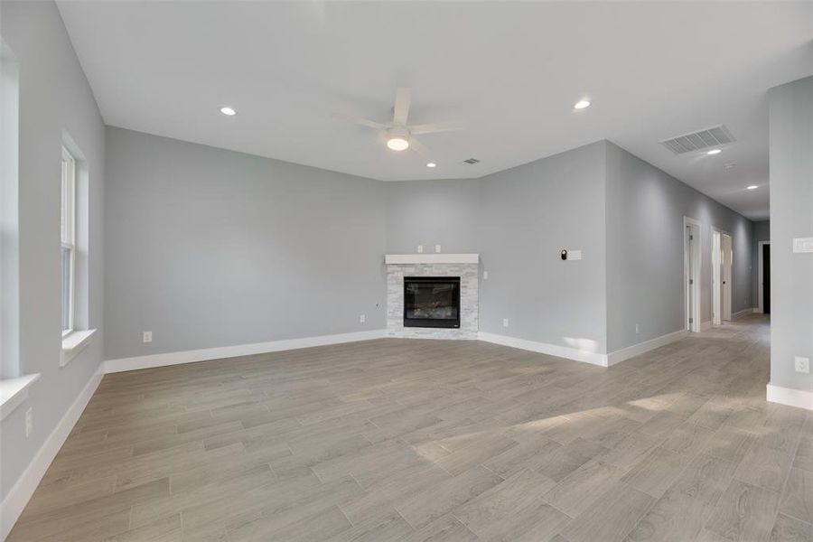 Unfurnished living room with a stone fireplace, light wood-type flooring, and ceiling fan