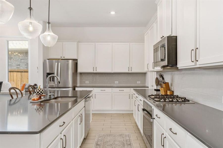 Kitchen featuring decorative backsplash, white cabinets, hanging light fixtures, appliances with stainless steel finishes, and sink