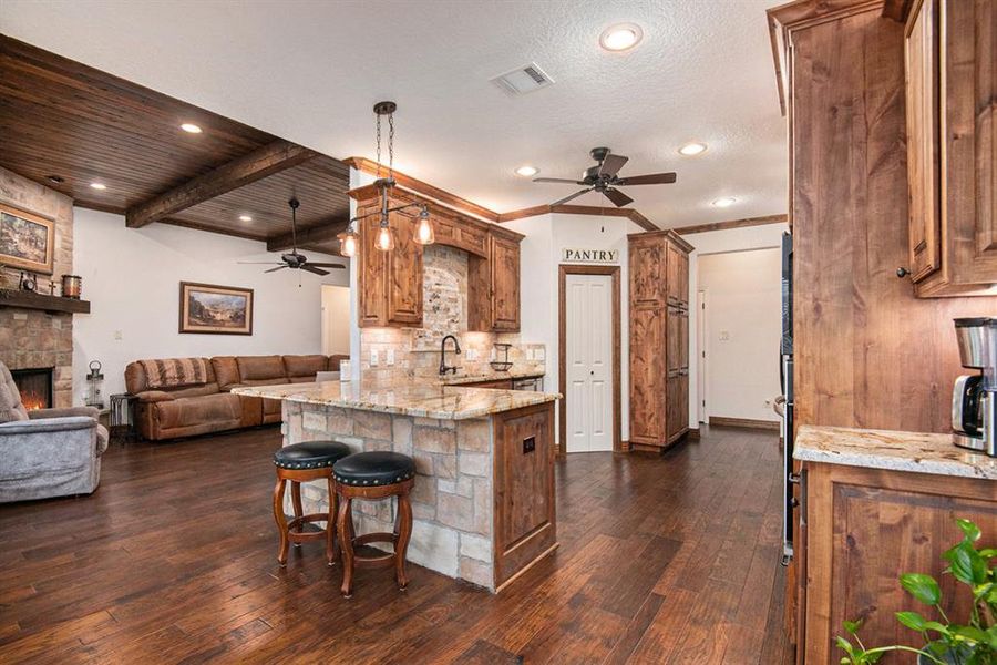 Kitchen with kitchen peninsula, light stone countertops, sink, and dark wood-type flooring