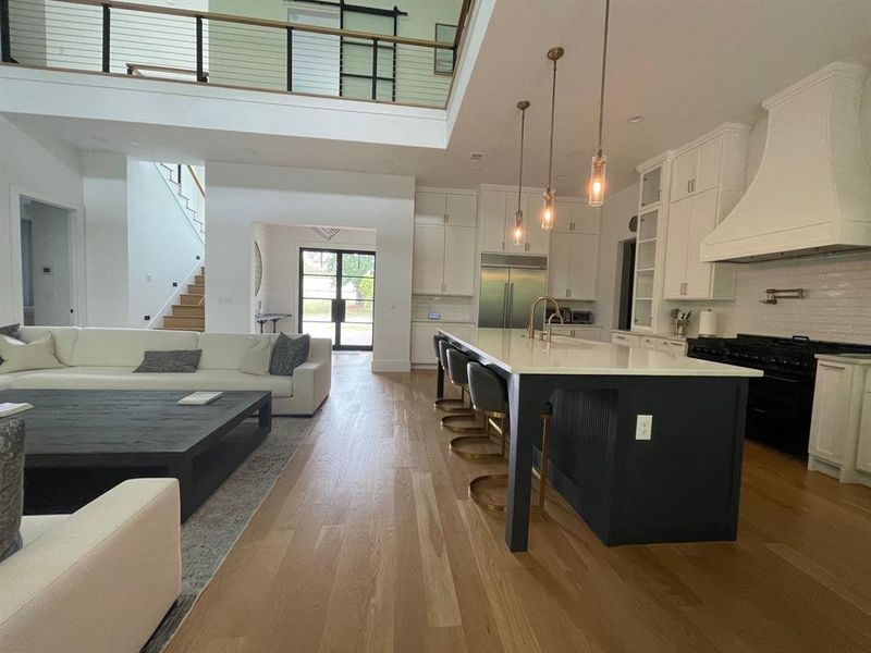 Kitchen featuring custom range hood, decorative backsplash, light hardwood / wood-style floors, a center island with sink, and premium appliances