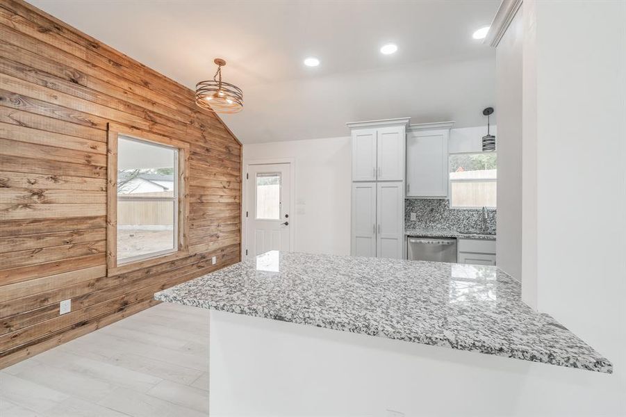 Kitchen with a wealth of natural light, wood walls, tasteful backsplash, and stainless steel dishwasher