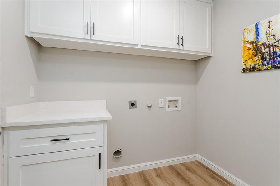 Clothes washing area featuring hookup for a gas dryer, hookup for a washing machine, hookup for an electric dryer, light wood-type flooring, and cabinets