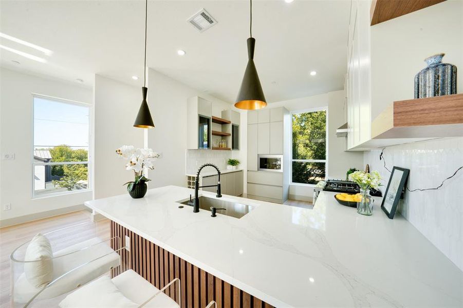 Kitchen with sink, white cabinets, hanging light fixtures, and light hardwood / wood-style flooring