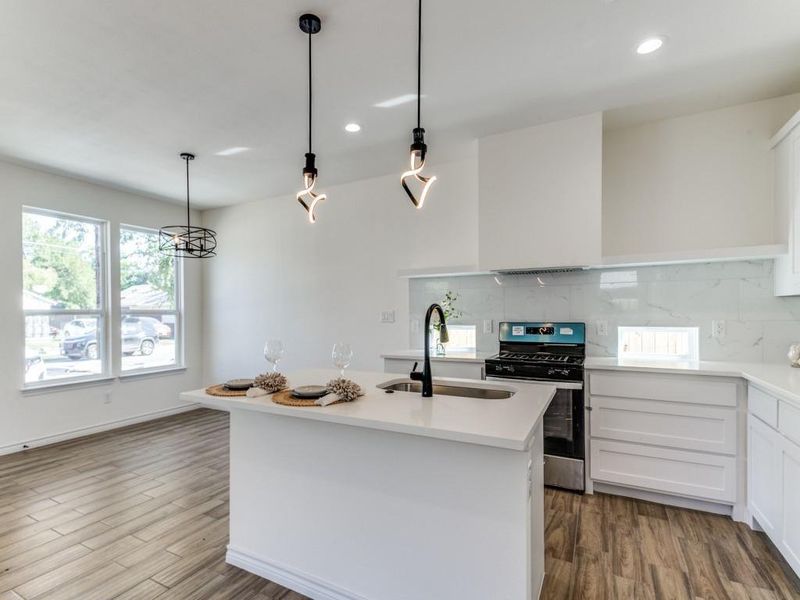 Kitchen with white cabinetry, a kitchen island with sink, wood-type flooring, stainless steel range with gas stovetop, and sink