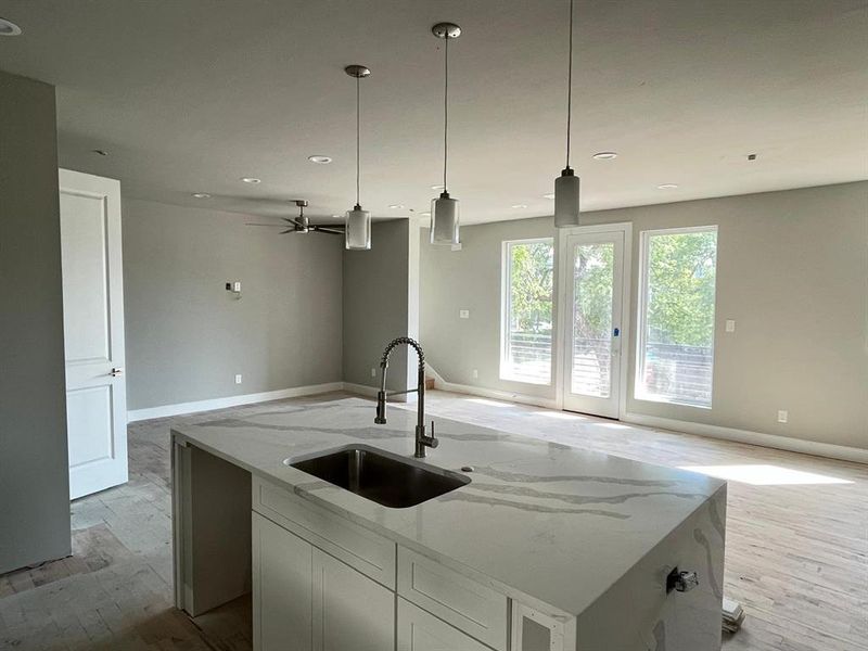 Kitchen with hanging light fixtures, a center island with sink, sink, and light stone countertops