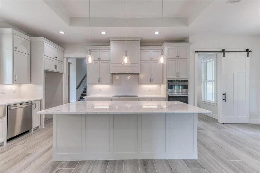 Kitchen with stainless steel appliances, decorative light fixtures, a kitchen island, and light stone countertops