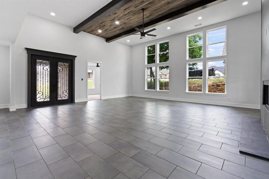 Unfurnished living room featuring plenty of natural light, ceiling fan, dark tile patterned flooring, and beam ceiling