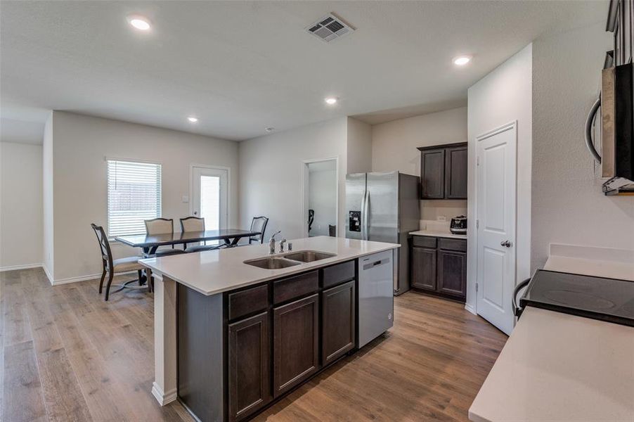 Kitchen with an island with sink, sink, dark brown cabinetry, appliances with stainless steel finishes, and light hardwood / wood-style floors