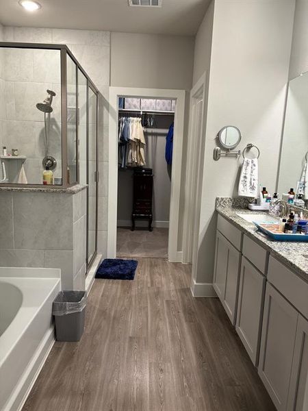 This is a modern bathroom featuring a walk-in shower, a double vanity with ample storage, and a walk-in closet. The space has a neutral color palette and laminate flooring.