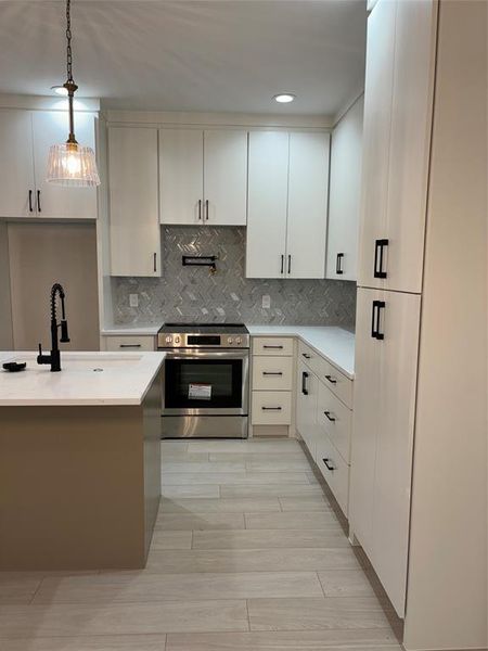 Kitchen featuring sink, backsplash, decorative light fixtures, stainless steel range, and white cabinets