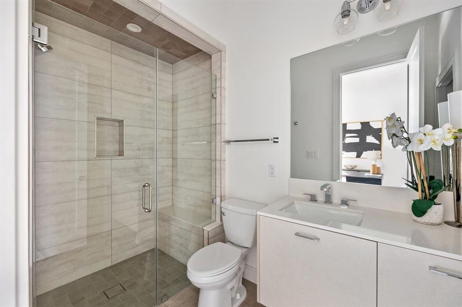 The ensuite bathroom features a frameless glass shower enclosures with matching hardware trim and wall of statement tile as well as vanity with under mount sink and storage.