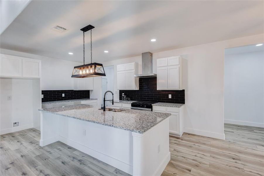 Kitchen with hanging light fixtures, a kitchen island with sink, wall chimney range hood, white cabinetry, and light wood-type flooring