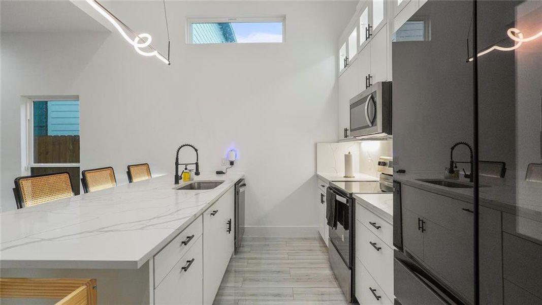 Kitchen featuring stainless steel appliances, white cabinets, sink, kitchen peninsula, and light stone countertops