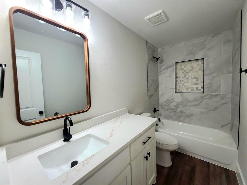 Guest bathroom with hardwood / wood-style floors, tiled shower / bath combo, toilet, and vanity