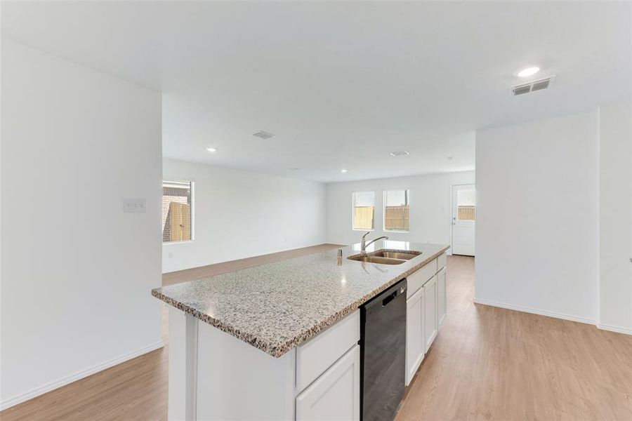 Kitchen with sink, dishwasher, white cabinetry, light hardwood / wood-style floors, and a kitchen island with sink