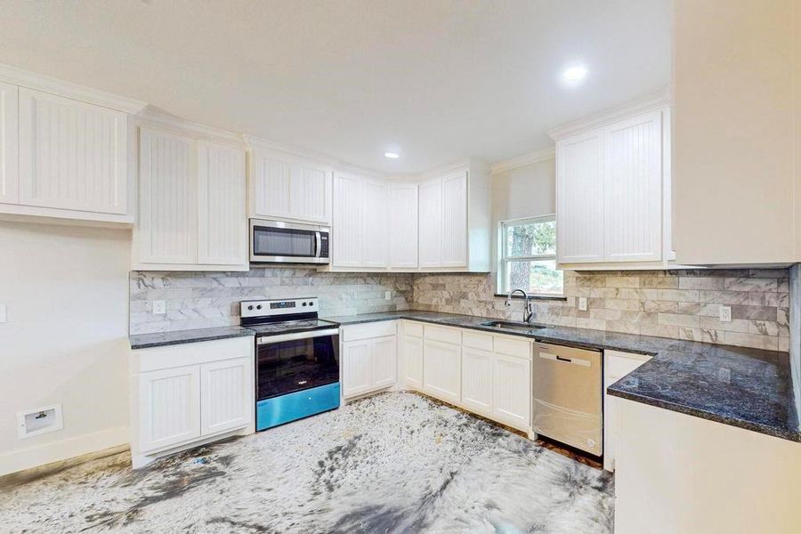 Kitchen featuring white cabinets, decorative backsplash, and appliances with stainless steel finishes