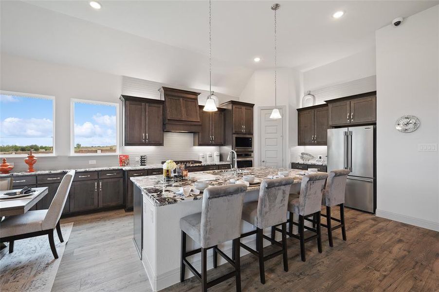 Kitchen with hardwood / wood-style flooring, custom range hood, stainless steel appliances, lofted ceiling, and an island with sink