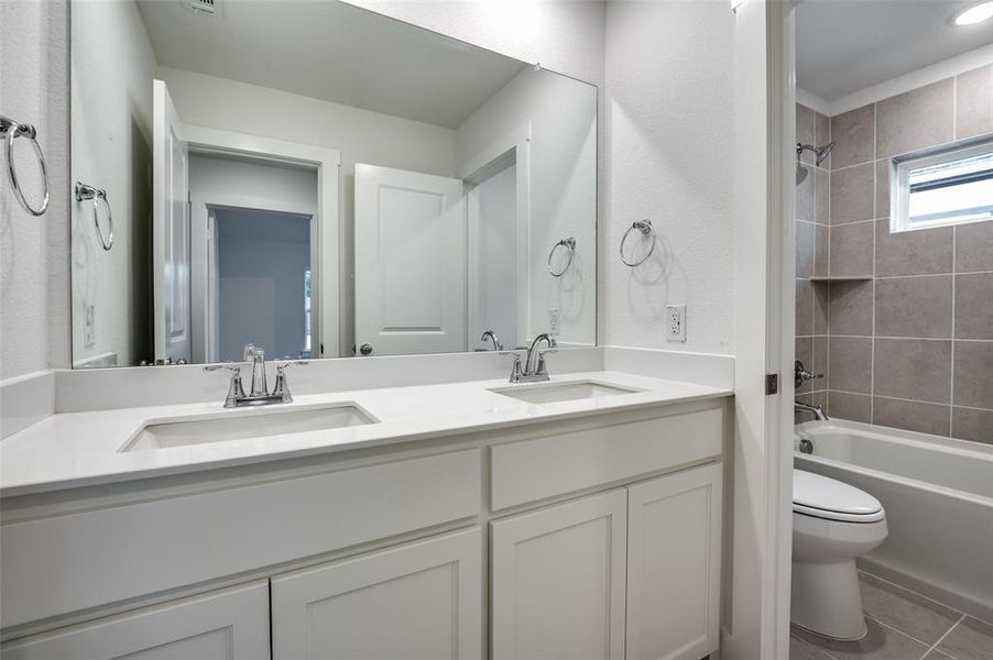 Full bathroom featuring tiled shower / bath, dual vanity, tile patterned flooring, and toilet