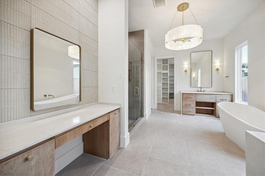Dual vanities and a dressing table are covered in natural quartzite. Exquisite lighting and the sparkle of brass fixtures and hardware provide timeless elegance. Luxury features such as an oversized shower and standalone, deep soaking tub complete the primary bath.