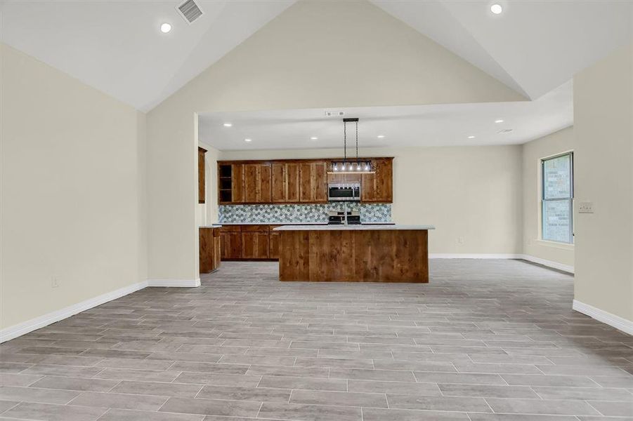 Kitchen with decorative light fixtures, stainless steel appliances, high vaulted ceiling, a center island, and backsplash