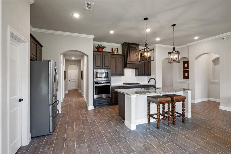 Kitchen with stainless steel appliances, hanging light fixtures, a kitchen island with sink, sink, and premium range hood