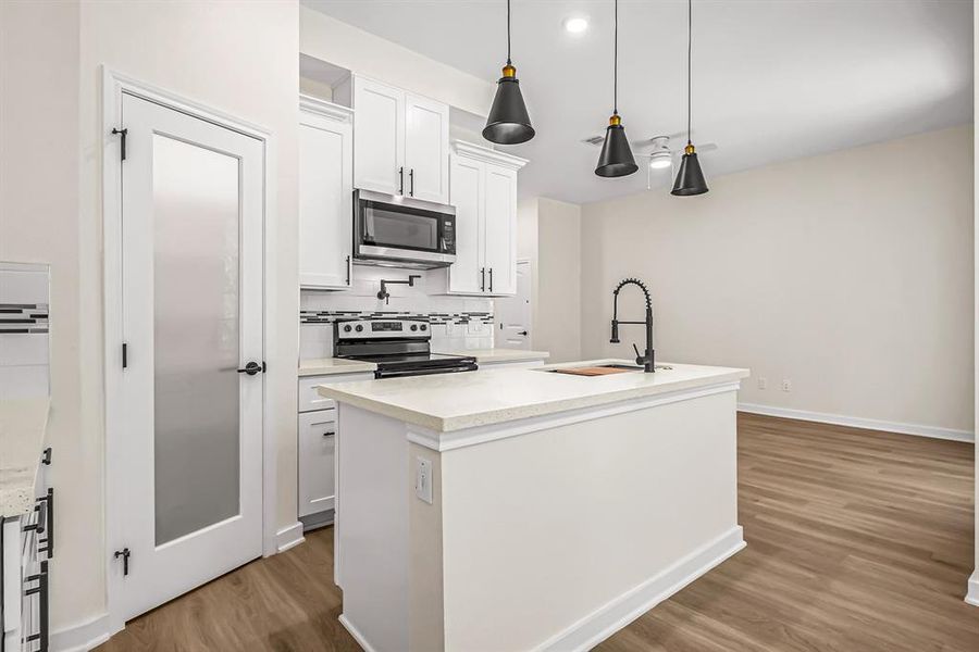 Kitchen is open to the living room beyond. Corner walk in pantry provides plenty f storage. Pot filler, designer tile backsplash and varied cabinet heights provide interest in this efficient kitchen.