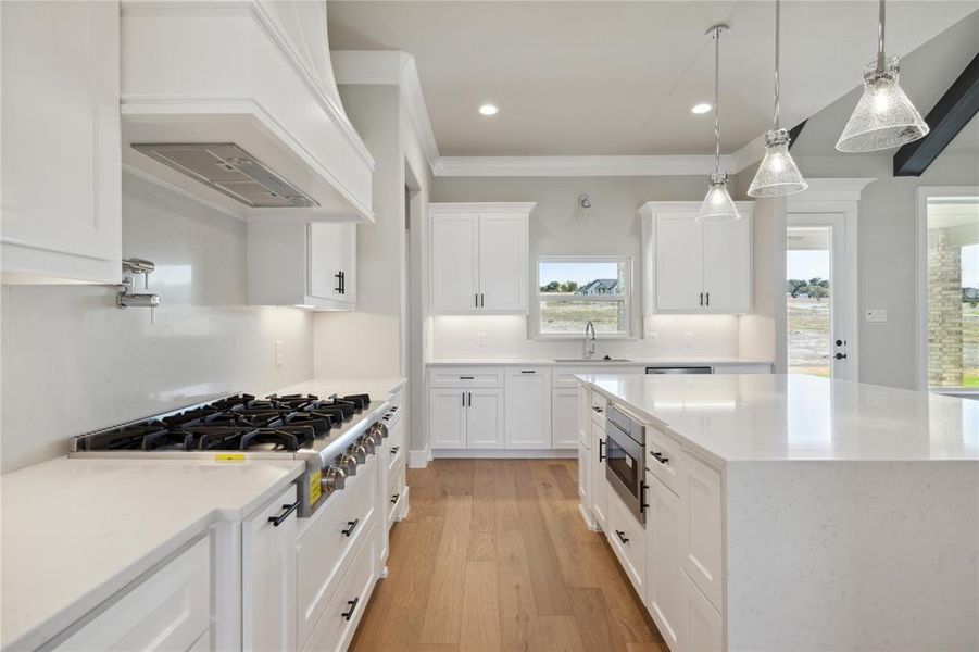 Kitchen with light hardwood / wood-style floors, white cabinetry, appliances with stainless steel finishes, ornamental molding, and premium range hood