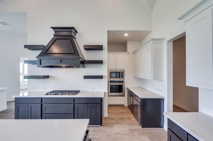 Kitchen with white cabinetry, light hardwood / wood-style floors, appliances with stainless steel finishes, a high ceiling, and custom exhaust hood