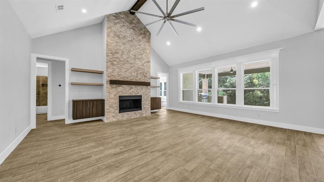 Unfurnished living room featuring ceiling fan, a stone fireplace, light wood-type flooring, and beam ceiling