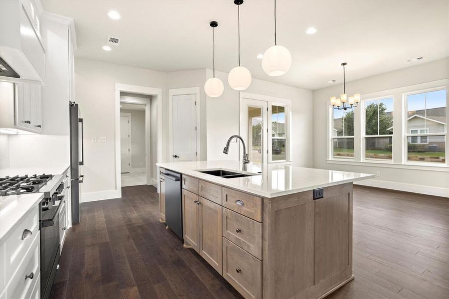 Kitchen with dark wood-type flooring, stainless steel appliances, a center island with sink, and white cabinets