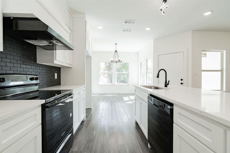 Kitchen with black appliances, sink, white cabinets, and hanging light fixtures