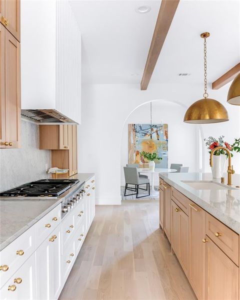 Kitchen with beam ceiling, sink, light wood-type flooring, hanging light fixtures, and light stone counters