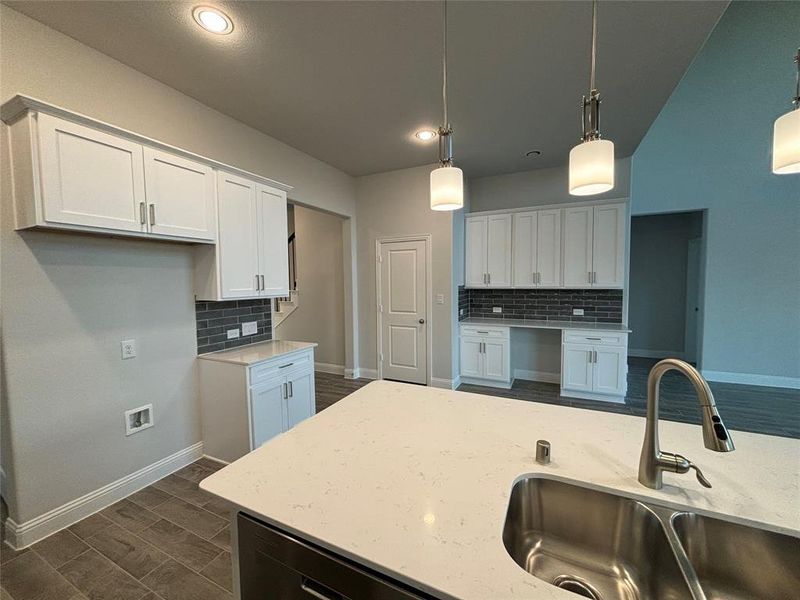 Kitchen with hanging light fixtures, light stone counters, backsplash, white cabinetry, and sink