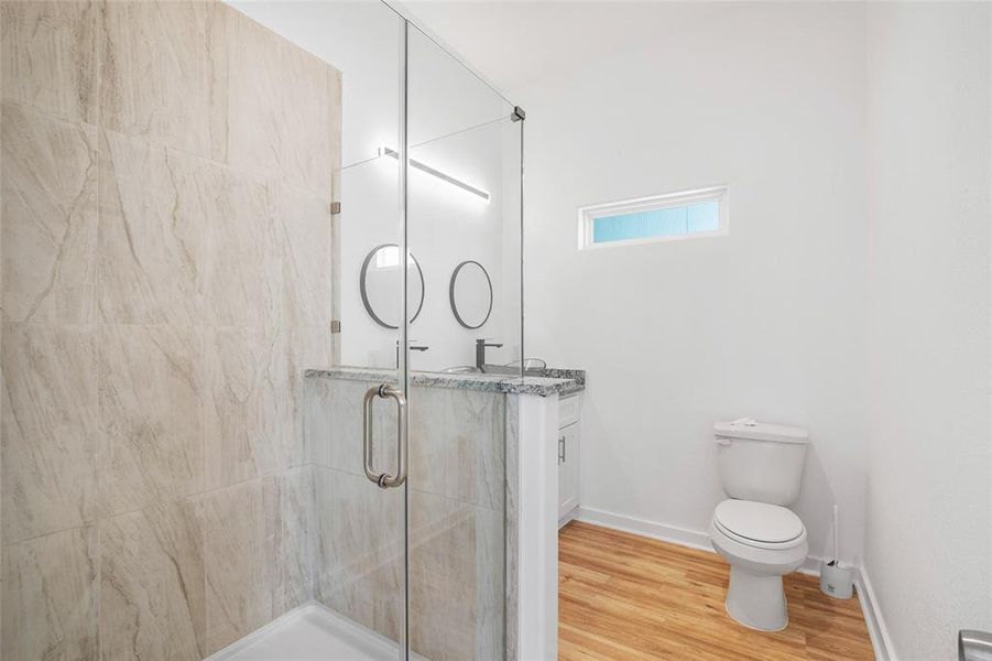 This is the modern primary bathroom with a glass-enclosed shower, a vanity with a granite countertop, and a small frosted window allowing for natural light.