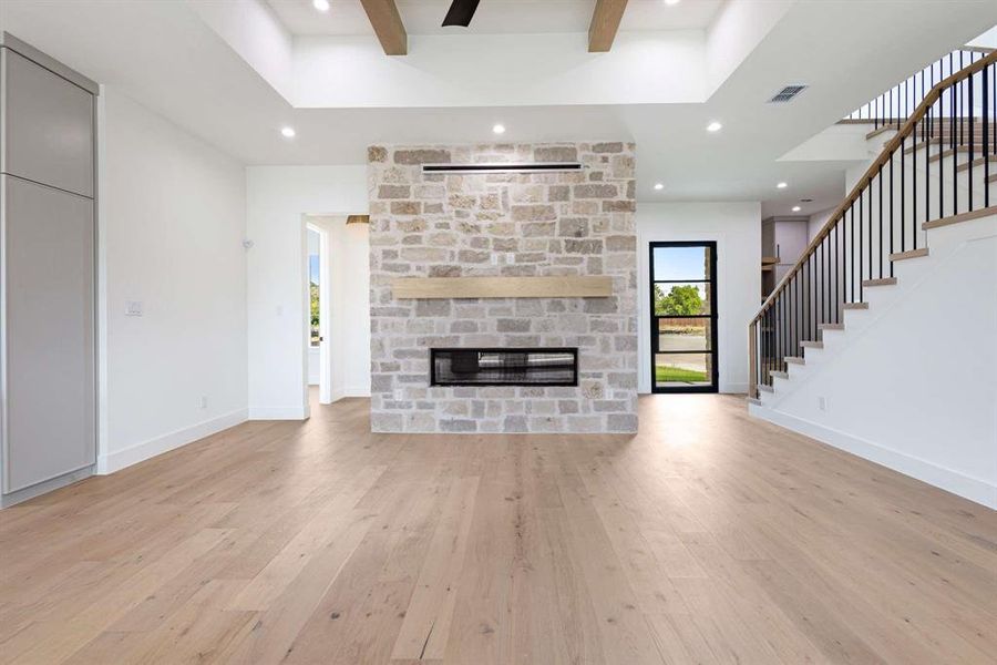 Unfurnished living room with a raised ceiling, a stone fireplace, and light hardwood / wood-style flooring