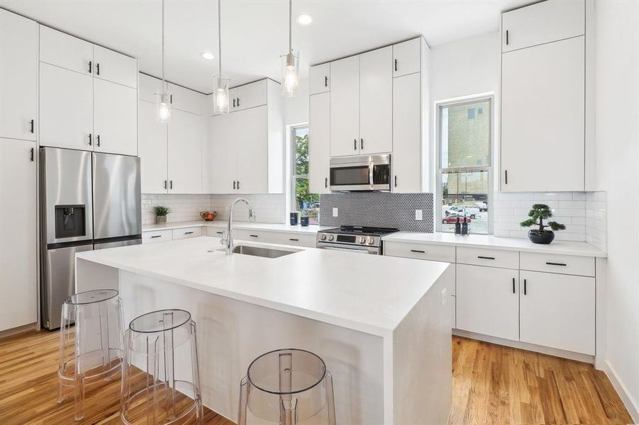 Kitchen with light wood-type flooring, appliances with stainless steel finishes, an island with sink, and sink