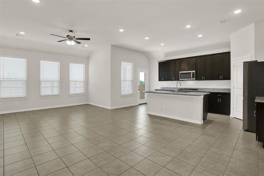 Kitchen with light tile floors, ceiling fan, a center island with sink, and fridge