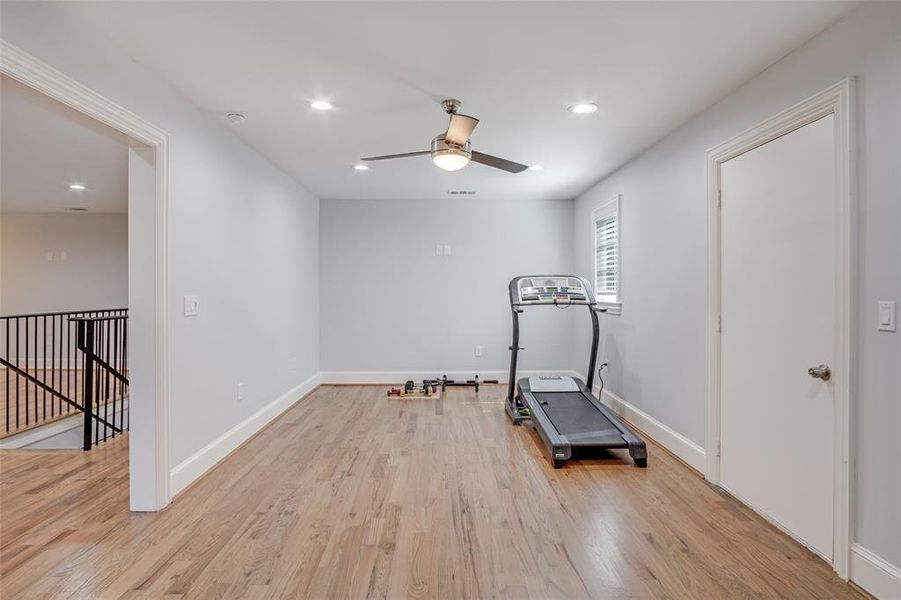 Exercise area with ceiling fan and light hardwood / wood-style flooring