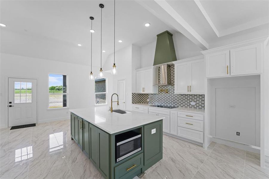 Kitchen featuring green cabinetry, a center island with sink, black electric cooktop, stainless steel microwave, and white cabinetry