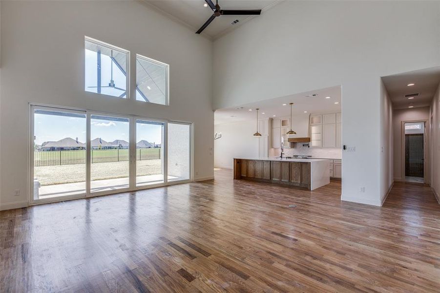 Unfurnished living room featuring ceiling fan, a towering ceiling, and hardwood / wood-style floors