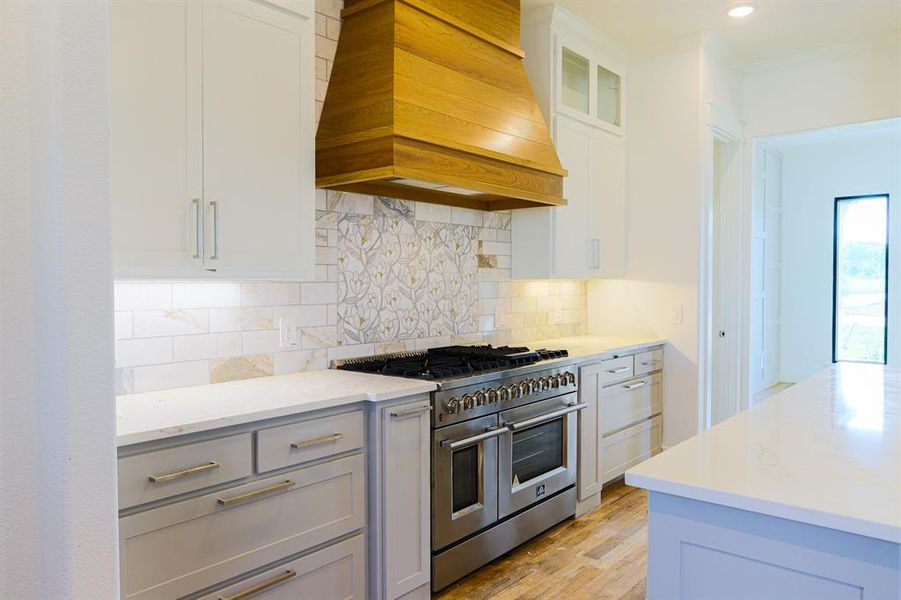 Kitchen featuring light hardwood / wood-style floors, range with two ovens, decorative backsplash, and custom range hood